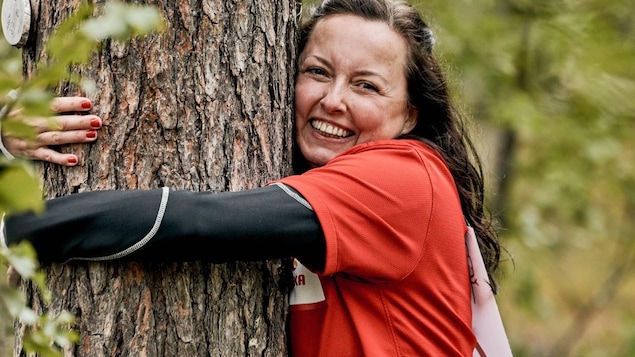 A woman smiles as she hugs a tree. 