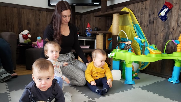 Trois enfants sur un tapis de jeu avec leur mère à l'arrière