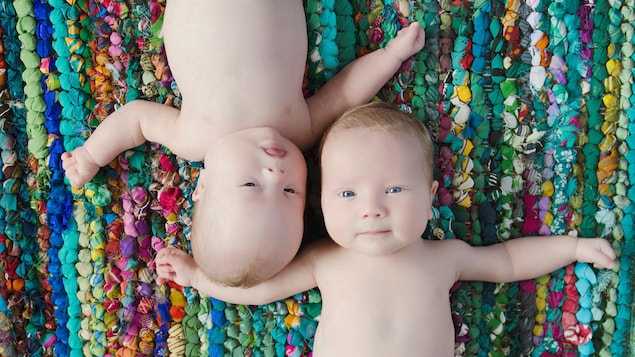 Deux bébés âgée de quelques mois sont couchés sur un tapis coloré
