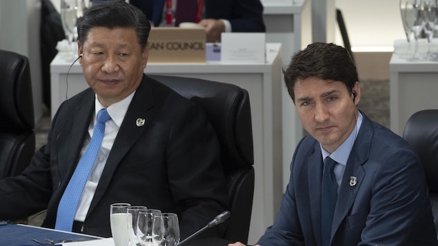 Justin Trudeau et Xi Jinping, qui portent des oreillettes, sont assis un à côté de l'autre dans une conférence internationale.