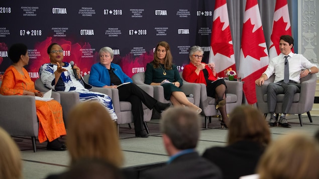 Des femmes, qui semblent être des panélistes, et un homme, qui semble animer la discussion, sont assis sur une scène.