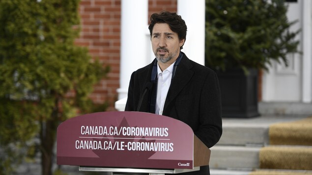 Plan moyen de Justin Trudeau derrière un micro, répondant à des questions.
