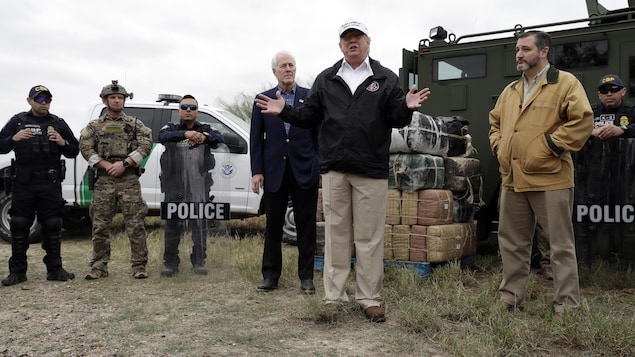 Donald Trump debout devant des véhicules des gardes frontaliers, en compagnie de six autres hommes, dont quatre en uniforme policier ou de camouflage.