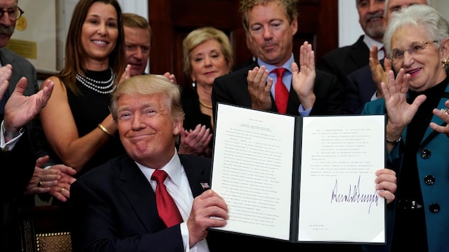Donald Trump, le sourire aux lèvres, montre le décret qu'il a signé jeudi à la Maison-Blanche et qui, selon lui, permettra à des millions d'Américains d'avoir une assurance maladie abordable.