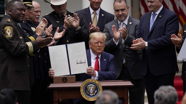 Donald Trump tient un décret dans ses mains et est applaudi par plusieurs personnes qui l'entourent.