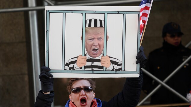 Une femme brandissant une pancarte représentant Trump derrière les barreaux. 