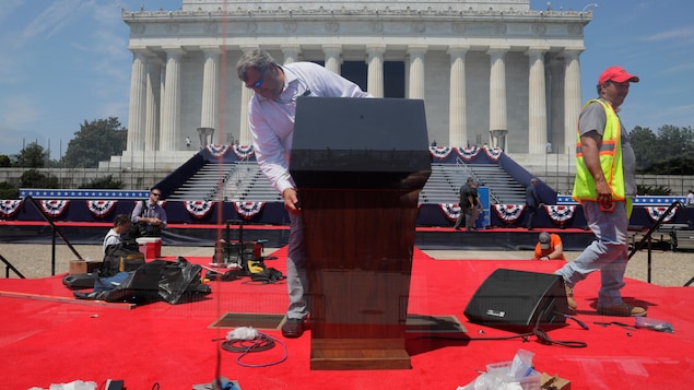 Un homme installe un lutrin sur un podium devant le monument.