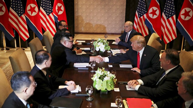 Kim Jong-un serre la main de Donald Trump, assis face à face à une longue table, entourés de trois proches conseillers chacun.