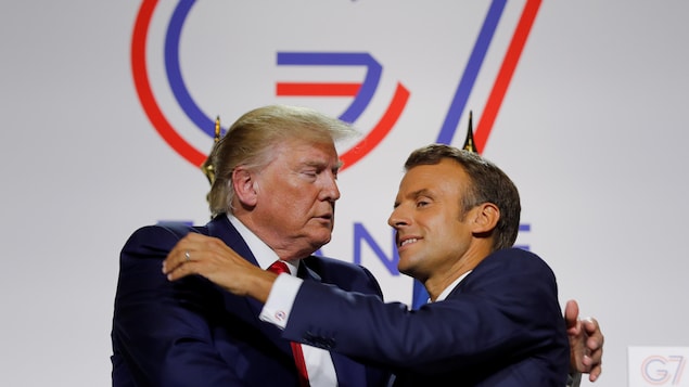 MM. Trump et Macron se donnent une accolade sous le logo de la rencontre du G7.
