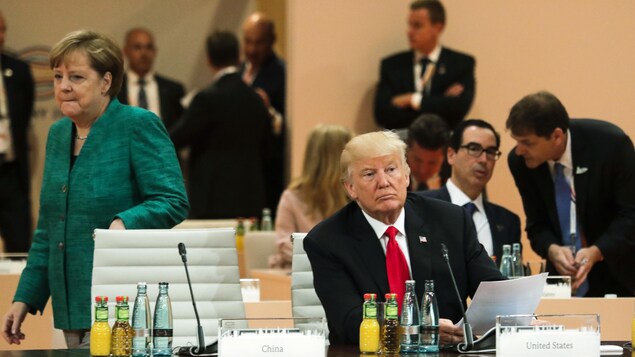 Donald Trump est assis seul alors que la chancelière allemande, Angela Merkel, marche derrière lui. Donald Trump est assis seul alors que la chancelière allemande, Angela Merkel, marche derrière lui.