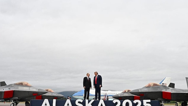 Two men stand on large podium with airplanes and jets in the background. 