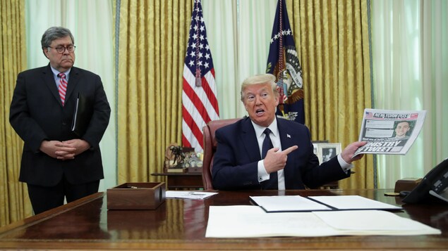 Donald Trump, assis, tenant une copie du New York Post pendant qu'il s'adresse aux reporters depuis le bureau ovale, avec à ses côtés Bill Barr.