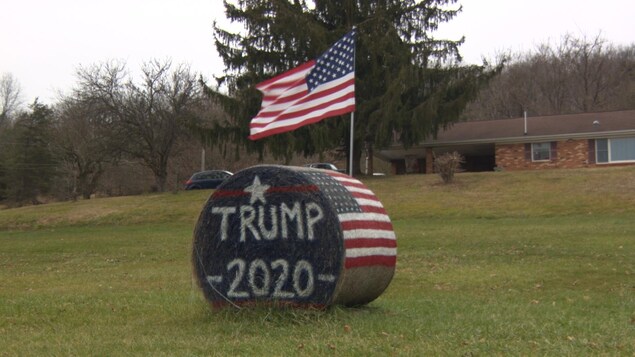 Au milieu d'un champ, une botte de foin aux couleurs du drapeau américain, sur laquelle est inscrit: Trump 2020.