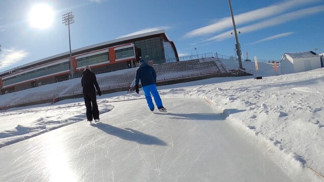 Deux patineurs glissent sur la piste d'athlétisme glacée du stade du PEPS de l'Université Laval. 