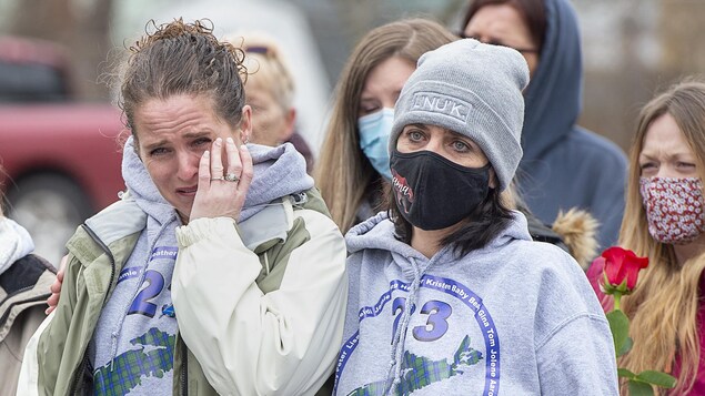 Une femme essuie ses larmes et est réconfortée par deux autres.