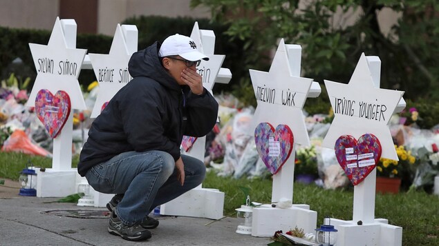Un homme est accroupi devant de petits monuments blancs surmontés d'étoiles de David, dans lesquelles sont inscrits les noms des victimes de la tuerie.