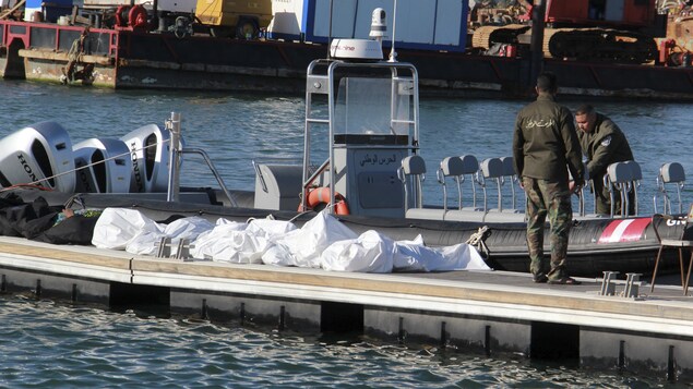 Des gardes cote se tiennent sur un quai flottant aux côtés de sacs mortuaires.