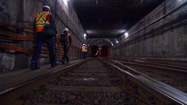 Des hommes vêtus de vestes réfléchissantes s'engouffrent dans le tunnel.