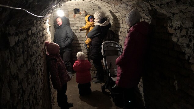 Un tunnel éclairé par une lampe, où s'abritent des adultes et des enfants.