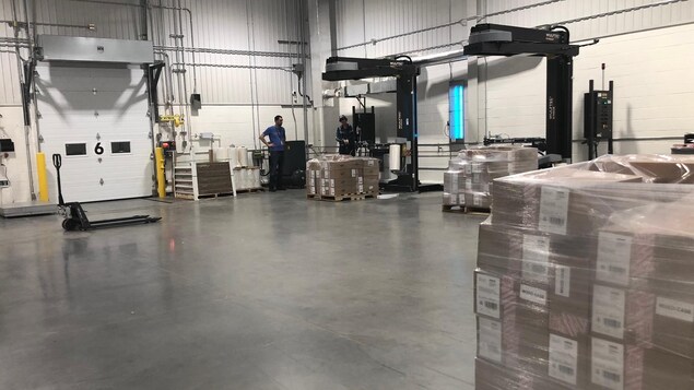 Des machines entourent des piles de boîtes, sous la supervision de deux employés. Des machines entourent des piles de boîtes, sous la supervision de deux employés.