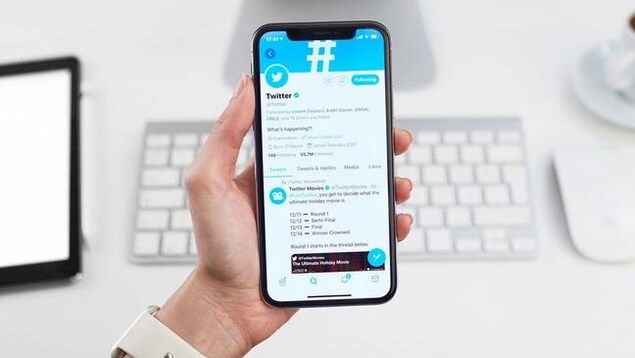 Une main tient un téléphone sur lequel s'affiche une page Twitter.