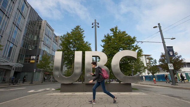 Une étudiante marche en regardant son téléphone en passant devant un signe qui dit UBC.