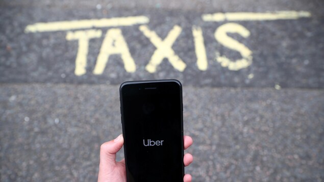 Un téléphone intelligent affichant l'application Uber, au-dessus d'une chaussée sur laquelle il est écrit : « TAXIS ».