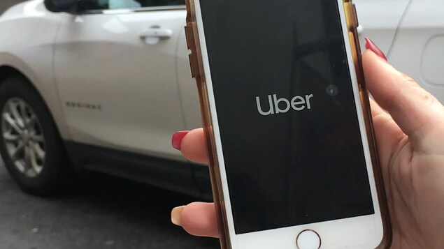 Une femme tient un téléphone intelligent sur lequel l'application d'Uber est en marche.