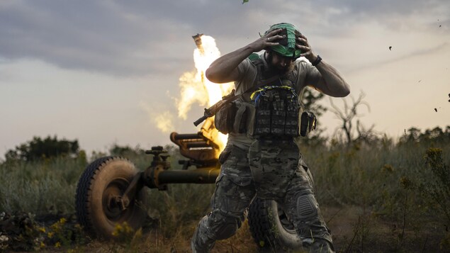 Un soldat tient son casque au moment du tir de mortier.
