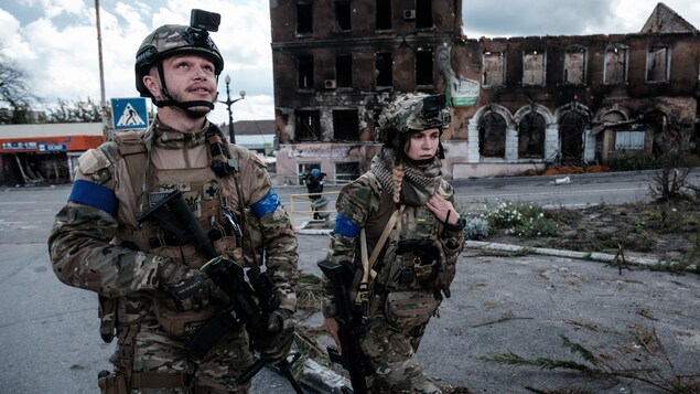 Deux soldats ukrainiens marchent sur une route jonchée de débris.