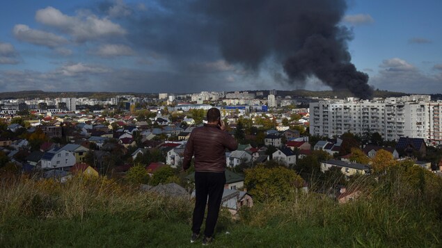 Un homme en surplomb regarde de la fumée s'élever de Lviv. 