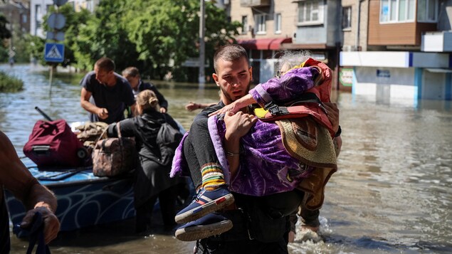 Un homme porte une vieille dame dans une zone inondée de Kherson.