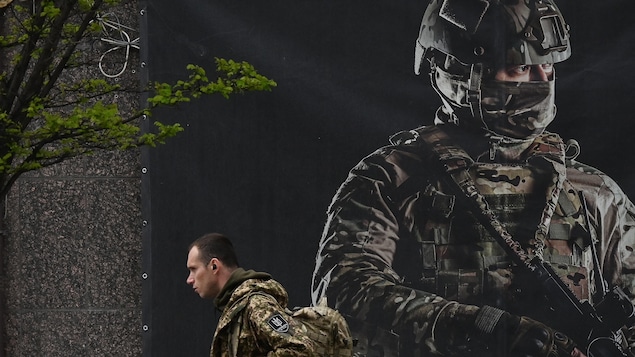 Un soldat en habit militare marche devant une grande affiche d'un soldat.