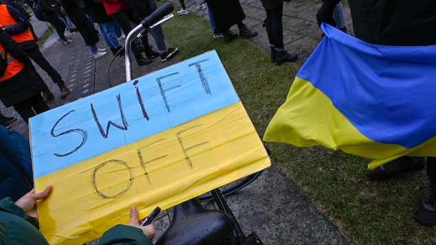 Un manifestant tient une pancarte sur laquelle on peut lire «SWIFT OFF».