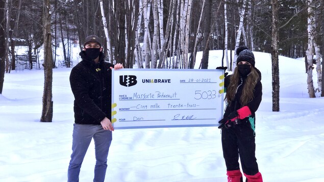 Un homme et une femme masqués tiennent un gros chèque dans une forêt l'hiver.
