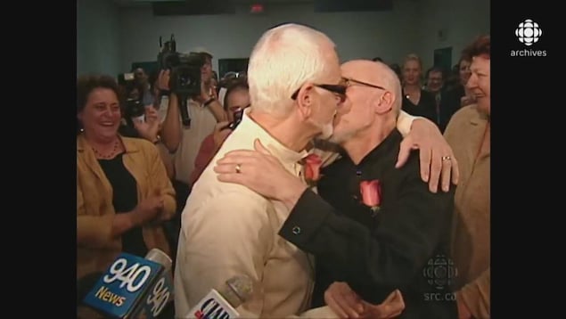 Theo Wouters et Roger Thibault s'embrassant sous le regard des caméras et d'amis souriants lors de leur cérémonie d'union civile