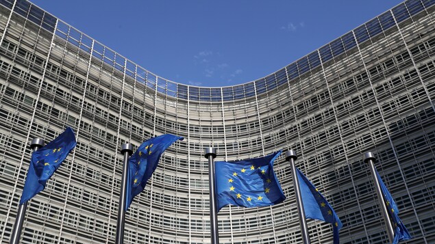 Cinq drapeaux de l'UE flottent devant un bâtiment concave à Bruxelles.