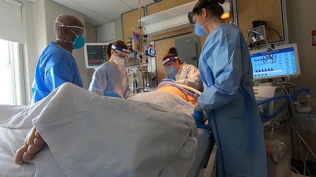 Quatre professionnels de la santé encerclent un patient des soins intensifs COVID placé en position ventrale et branché à un respirateur artificiel.