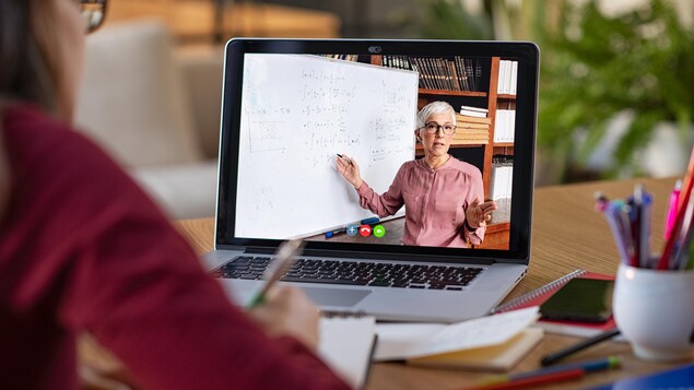 Un ordinateur portable ouvert. On voit à l'écran une professeure d'université donnant un cours.