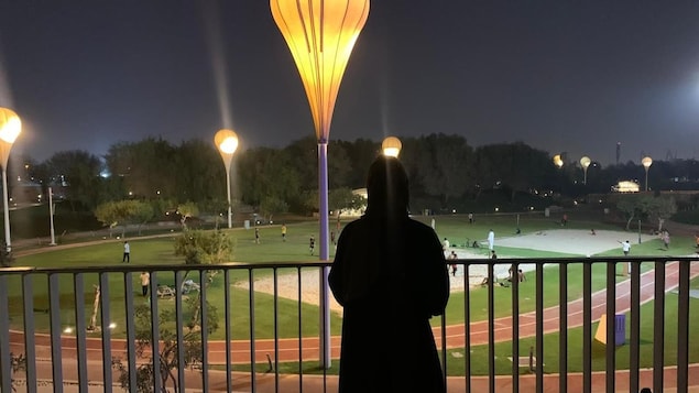 A young woman looking at a sports pitch at night.
