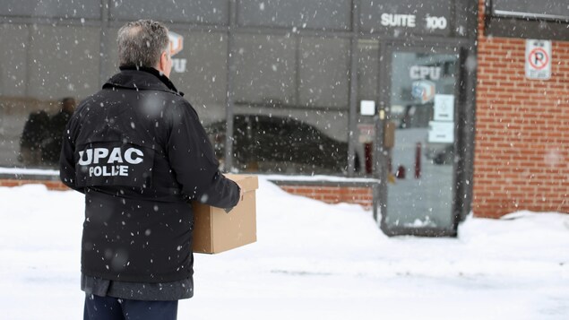 Un enquêteur de l'UPAC tient une boîte dans ses mains à proximité des bureaux d'une entreprise. Un enquêteur de l'UPAC tient une boîte dans ses mains à proximité des bureaux d'une entreprise.