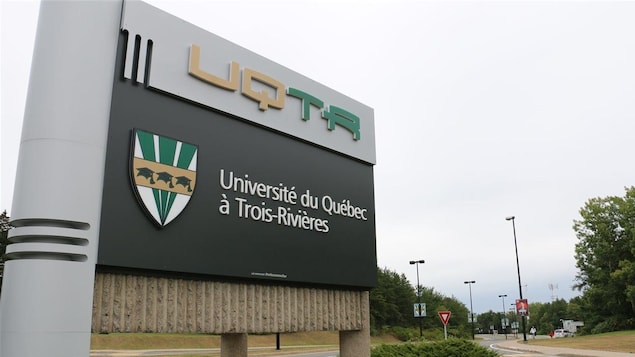 Pancarte à l'entrée du campus de l'UQTR devant des arbres feuillus.