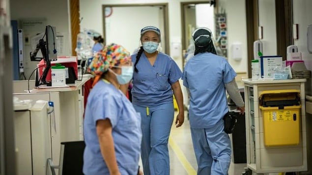 Trois infirmières portant des masques qui marchent dans un hôpital.
