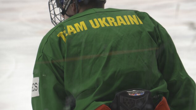 Un joueur sur la patinoire de dos avec un chandail sur lequel est écrit « Équipe Ukraine » en anglais.  