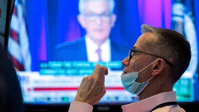 A trader watches Federal Reserve chair Jerome Powell speak about the U.S. central bank's latest policy decision in the midst of the ongoing COVID-19 pandemic. Global stock markets and oil prices fell Friday on news of a new coronavirus variant in South Africa and a return of travel restrictions in parts of the EU.