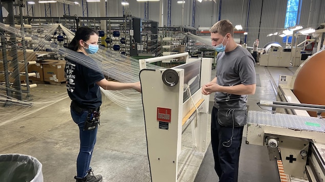 Deux employés se tiennent près d'une machine dans une usine de fabrication de textiles.