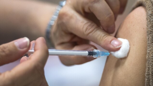 Une personne injecte une dose de vaccin dans un bras.