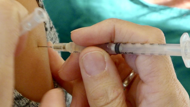 Une seringue de vaccination pénètre un bras.
