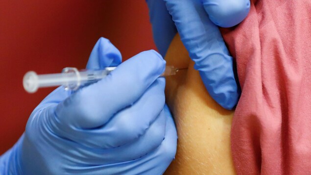 Gros plan sur l'injection d'un vaccin dans un bras par une personne aux mains gantées.