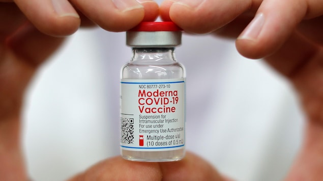 Two hands holding a vial of Moderna COVID-19 vaccine.